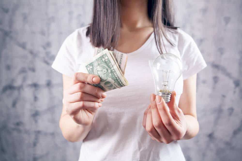 Woman holding dollar bills in one hand and a light bulb in the other.