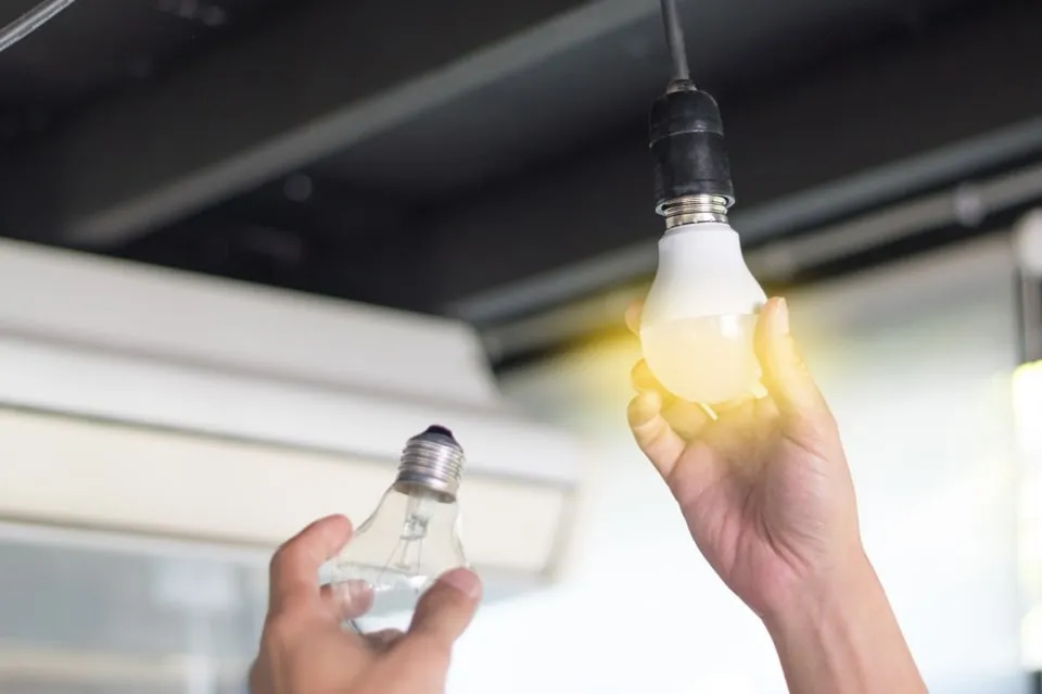 Person replacing an old light bulb with a new glowing LED bulb.