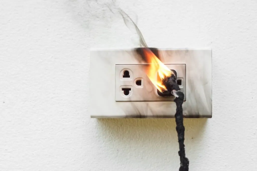 Electrical outlet on fire with a burning cord and smoke damage.