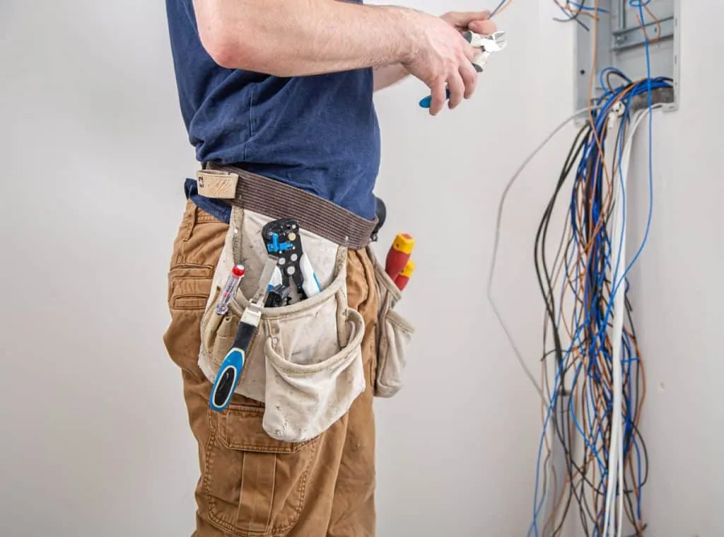 Electrician with tool belt working on a wall panel full of wires.