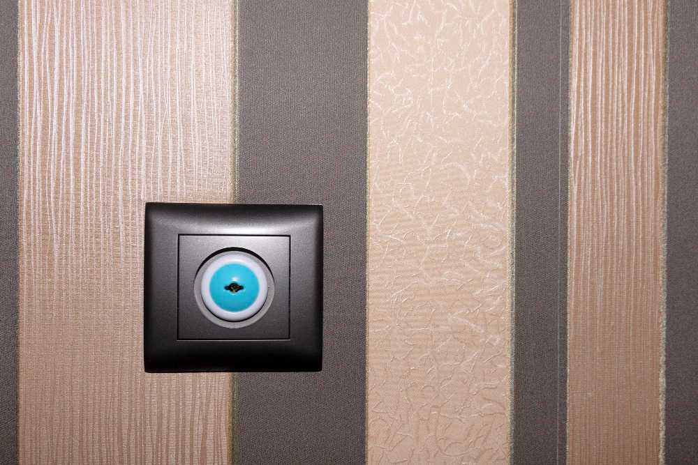 Close-up of a modern, black circular wall outlet or switch on striped wallpaper.