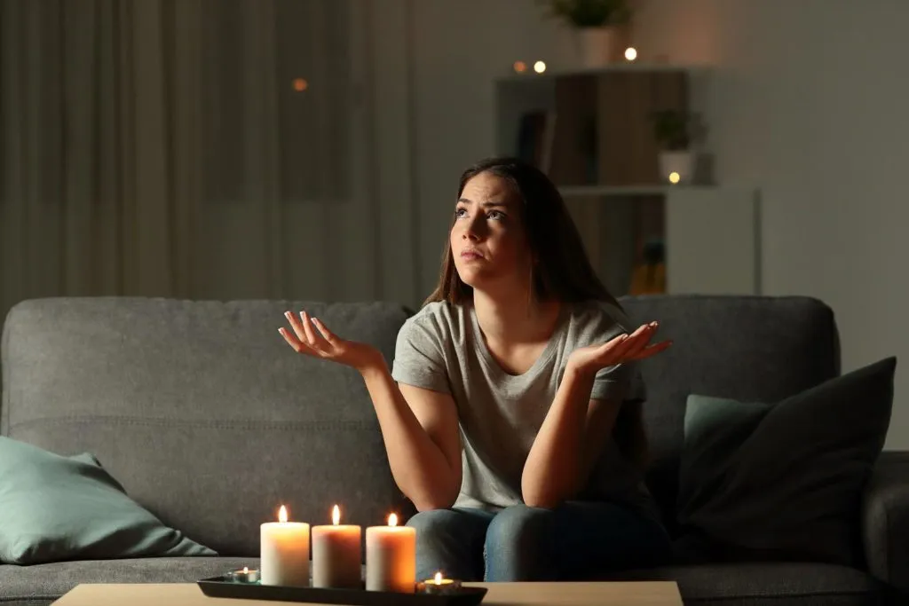 Woman sitting on a couch with candles during a power outage, looking confused.