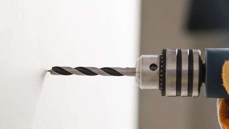 Close-up of a power drill making a hole in a white wall.