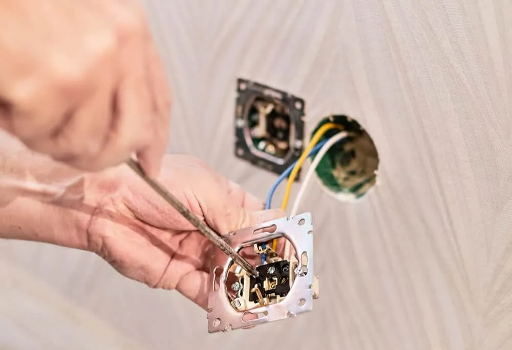 Person using a screwdriver to install or repair electrical wiring in a wall outlet.