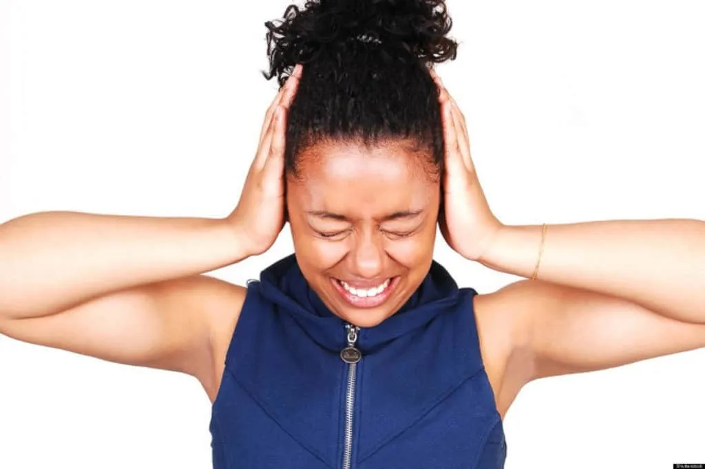 Woman closing her eyes and covering her ears due to loud noise or discomfort.