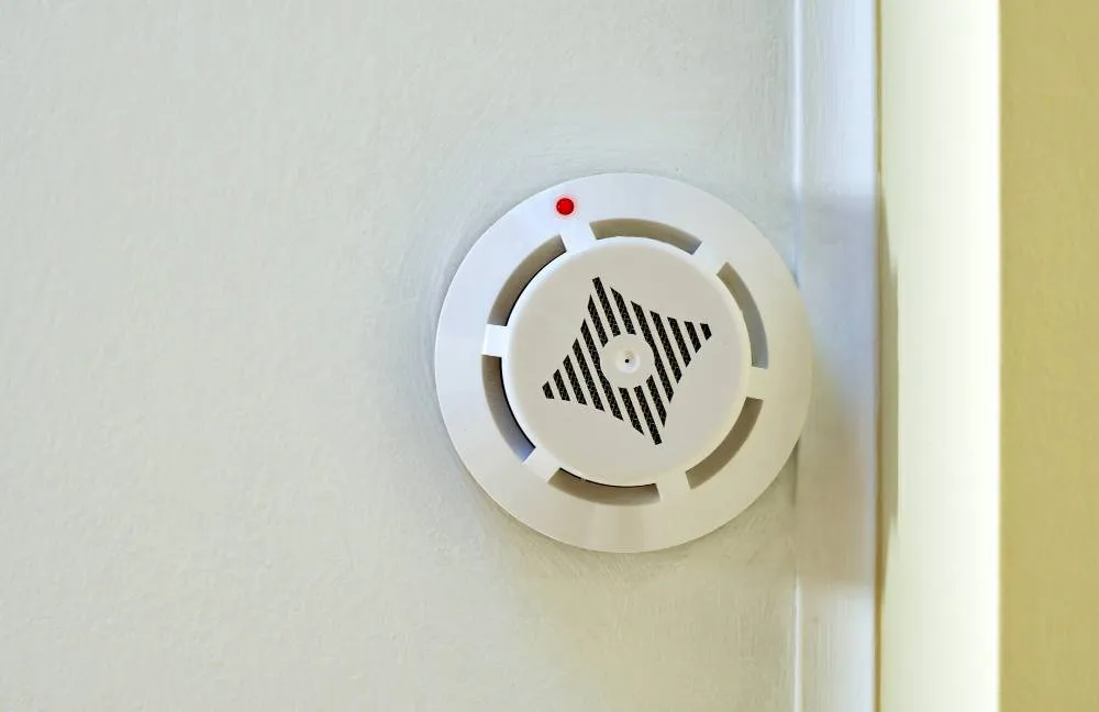 Wall-mounted smoke detector with a red indicator light.