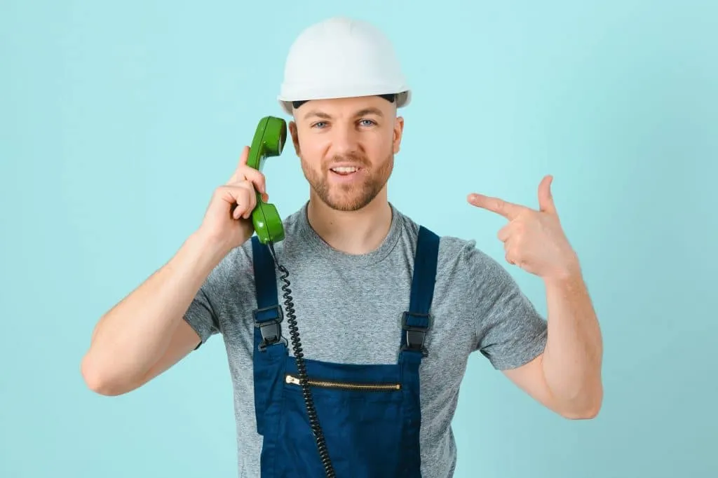 Smiling construction worker in a hard hat talking on a green corded phone.