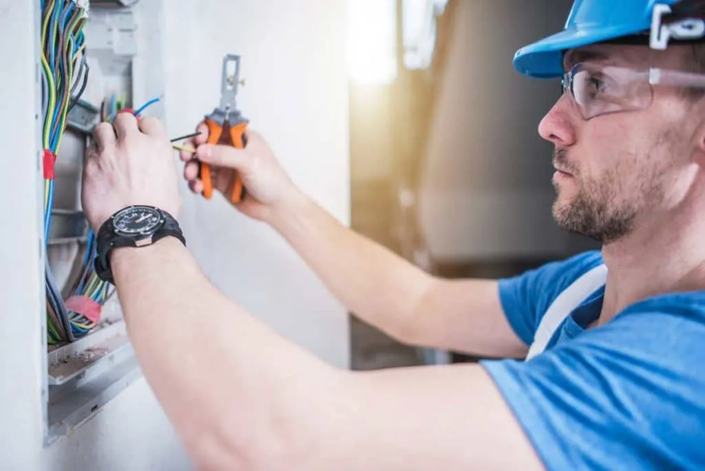 Electrician working on electrical wiring in a panel wearing a blue hard hat.