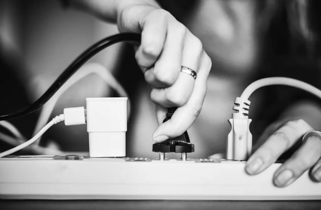 Close-up of a person plugging a power cord into a power strip.